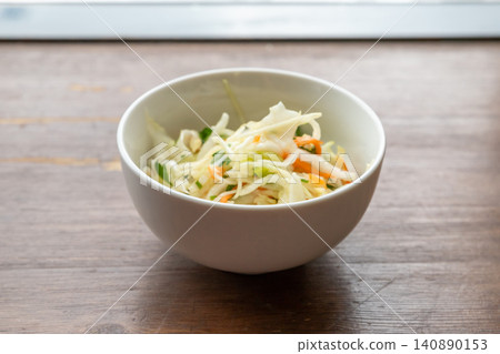 Sauerkraut in white bowl on wooden table. Fermented cabbage salad with carrot. Traditional healthy probiotic food. Organic vegetable dish for nutrition and gut health concept. Sauerkraut in white bowl on wooden table. Fermented cabbage salad with carrot. Traditional healthy probiotic food. Organic vegetable dish for nutrition and gut health concept. 140890153