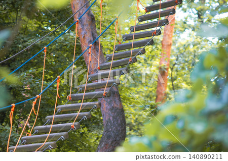 Rope park suspension bridge with dark wooden steps in summer forest Rope park suspension bridge with dark wooden steps in summer forest 140890211