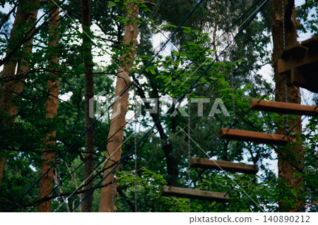 Rope park suspension bridge with wooden steps in a green forest Rope park suspension bridge with wooden steps in a green forest 140890212