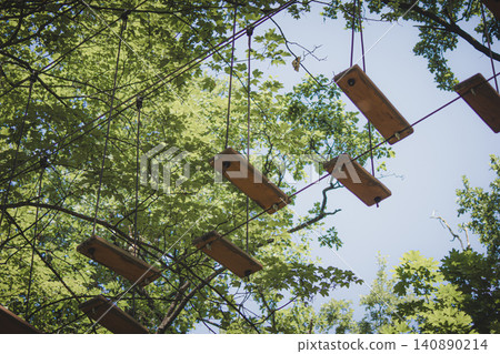 Suspended wooden steps of an obstacle course against green forest canopy 140890214
