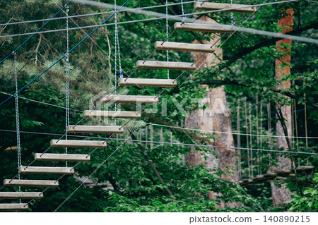 Suspension rope bridge with wooden steps in an outdoor adventure park Suspension rope bridge with wooden steps in an outdoor adventure park 140890215