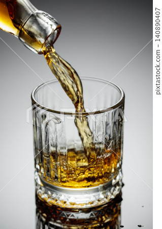 The amber-gold strong alcoholic beverage is poured into a glass. The amber-gold strong alcoholic beverage is poured into a glass. 140890407