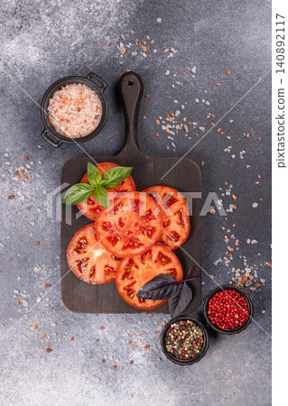 Sliced red tomatoes with basil, salt, and peppercorns on dark board Sliced red tomatoes with basil, salt, and peppercorns on dark board 140892117