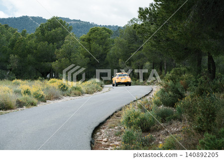 Yellow sports car driving on scenic forest road with mountain view Yellow sports car driving on scenic forest road with mountain view 140892205