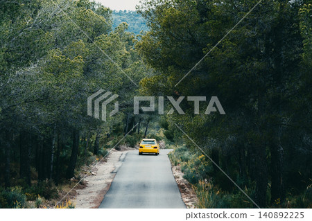 Yellow car driving through a forest road surrounded by lush greenery Yellow car driving through a forest road surrounded by lush greenery 140892225