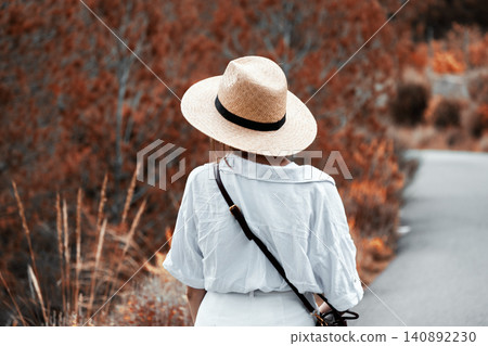 Woman in straw hat exploring autumn pathway in casual attire 140892230