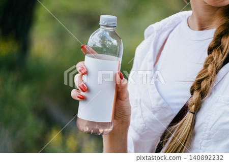 Woman holding blank water bottle in outdoor setting for branding concept Woman holding blank water bottle in outdoor setting for branding concept 140892232