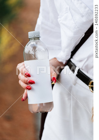 Woman holding recyclable water bottle with blank label in outdoor setting Woman holding recyclable water bottle with blank label in outdoor setting 140892233