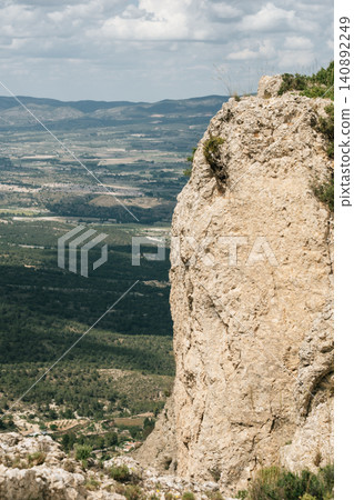 Majestic mountain cliff overlooking expansive valley under cloudy sky Majestic mountain cliff overlooking expansive valley under cloudy sky 140892249