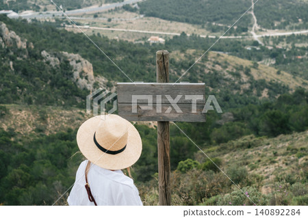 Woman in straw hat reading blank signboard in mountainous landscape Woman in straw hat reading blank signboard in mountainous landscape 140892284