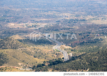 Aerial view of winding highway through rugged hills and expansive landscape on a sunny day 140892391