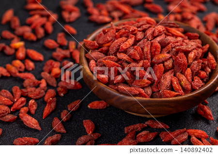 Dried goji berries overflowing a wooden bowl on a dark background Dried goji berries overflowing a wooden bowl on a dark background 140892402