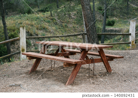 Rustic wooden picnic table in serene forest setting with lush greenery Rustic wooden picnic table in serene forest setting with lush greenery 140892431