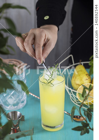 Real woman preparing Pear Collins Cocktail in highball glass or mocktails surrounded by ingredients and bar tools on turquoise table surface Real woman preparing Pear Collins Cocktail in highball glass or mocktails surrounded by ingredients and bar tools on turquoise table surface 140892544