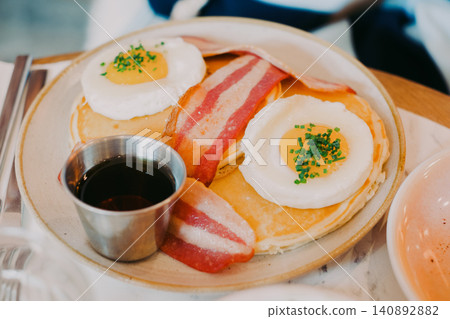 Delicious breakfast spread with pancakes, fried eggs, bacon, and syrup on a plate Delicious breakfast spread with pancakes, fried eggs, bacon, and syrup on a plate 140892882