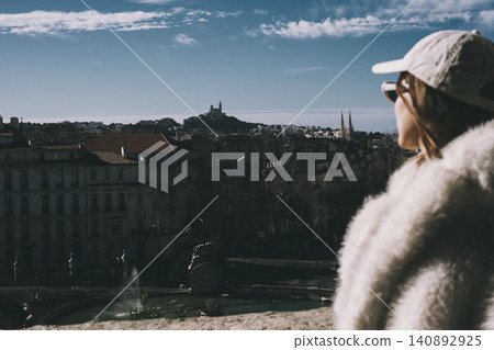 Scenic urban view of marseille with woman in winter outfit gazing from rooftop terrace Scenic urban view of marseille with woman in winter outfit gazing from rooftop terrace 140892925