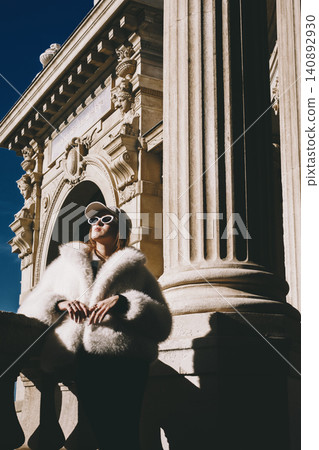 Chic woman in fur coat and sunglasses standing by historic architecture Chic woman in fur coat and sunglasses standing by historic architecture 140892930