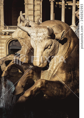 Historic bull statue fountain with majestic architecture in sunlight Historic bull statue fountain with majestic architecture in sunlight 140892993