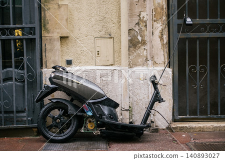 Abandoned electric scooter missing front wheel parked against weathered urban wall Abandoned electric scooter missing front wheel parked against weathered urban wall 140893027