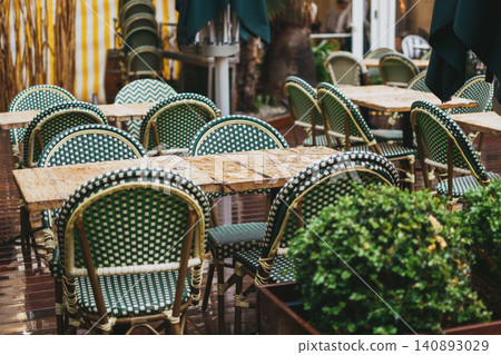 Charming outdoor cafe scene with woven chairs and rustic wooden tables in a cozy patio setting Charming outdoor cafe scene with woven chairs and rustic wooden tables in a cozy patio setting 140893029