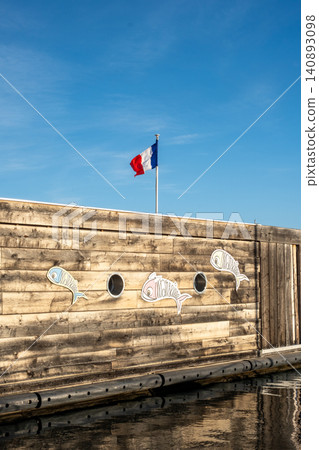 Rustic wooden building by french coastal waterfront with painted fish and blue sky 140893098