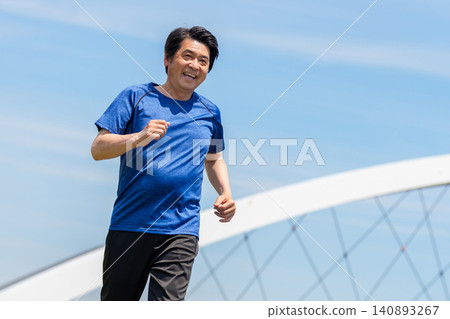 A senior man is jogging with a smile under the blue sky. A senior man is jogging with a smile under the blue sky. 140893267