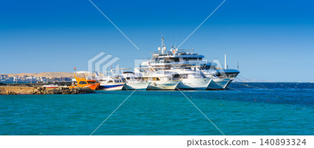 Hurghada, Egypt - Mar 3 2023, panoramic view of the bay and pier with luxury and expensive yachts and boats moored, in the daytime, on the beach of Hurghada, Egypt Hurghada, Egypt - Mar 3 2023, panoramic view of the bay and pier with luxury and expensive yachts and boats moored, in the daytime, on the beach of Hurghada, Egypt 140893324