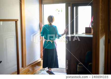 The back view of a woman holding a broom at the entrance. The back view of a woman holding a broom at the entrance. 140894103