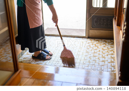A woman sweeping the entrance floor with a broom. A woman sweeping the entrance floor with a broom. 140894118