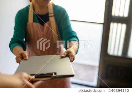 A woman in an apron hands over some documents. A woman in an apron hands over some documents. 140894120
