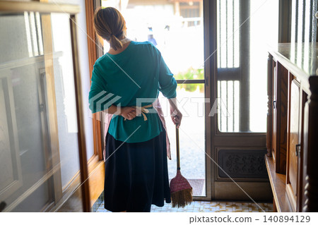 一位女子站在入口處，手裡拿著一把掃帚。 140894129