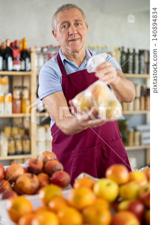 Mature salesman giving apples in grocery store Mature salesman giving apples in grocery store 140894834
