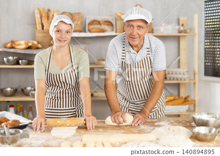 Man and woman bakers roll out dough with rolling pin Man and woman bakers roll out dough with rolling pin 140894895