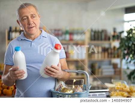 Mature man is choosing bottled milk in grocery store Mature man is choosing bottled milk in grocery store 140894907