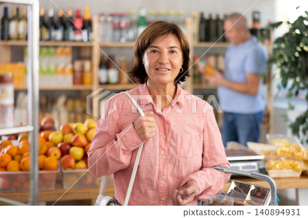 Visiting store, elderly woman is looking at something on shelf of showcase. Man buyer in background Visiting store, elderly woman is looking at something on shelf of showcase. Man buyer in background 140894931