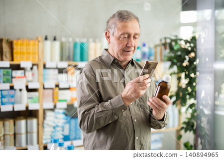 Senior man checking syrup medicine details on smartphone Senior man checking syrup medicine details on smartphone 140894965
