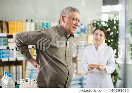 Man with back pain choosing pills with help of pharmacist Man with back pain choosing pills with help of pharmacist 140895013