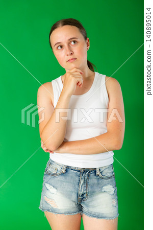 Teen european girl dressed in stylish shorts standing with thoughtful and sad-think look against green screen, chroma key compositing Teen european girl dressed in stylish shorts standing with thoughtful and sad-think look against green screen, chroma key compositing 140895014