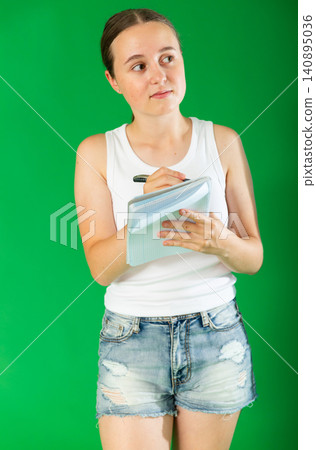 Teenage girl writing in notebook with pen in front of green screen Teenage girl writing in notebook with pen in front of green screen 140895036
