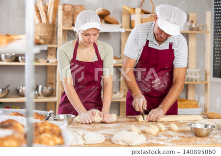 Male and female bakers kneading and cutting dough Male and female bakers kneading and cutting dough 140895060