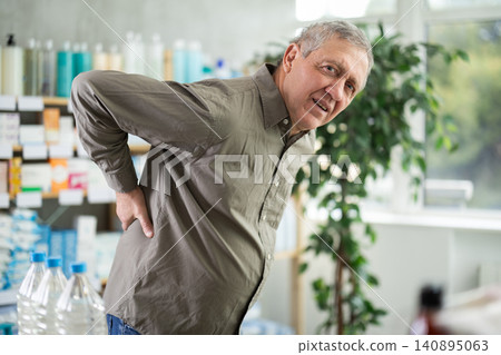 Elderly man holding his back in a pharmacy Elderly man holding his back in a pharmacy 140895063