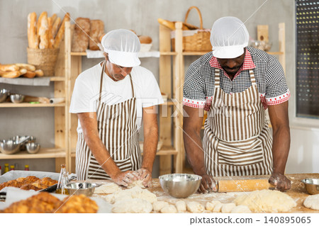 Two bakers working to knead and roll dough in bakery Two bakers working to knead and roll dough in bakery 140895065