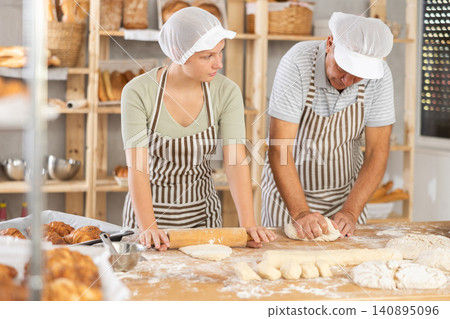 Man and woman bakers roll out dough with rolling pin Man and woman bakers roll out dough with rolling pin 140895096