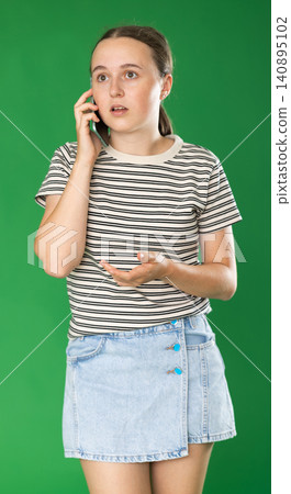 Teenage girl talking on mobile phone in front of green screen Teenage girl talking on mobile phone in front of green screen 140895102