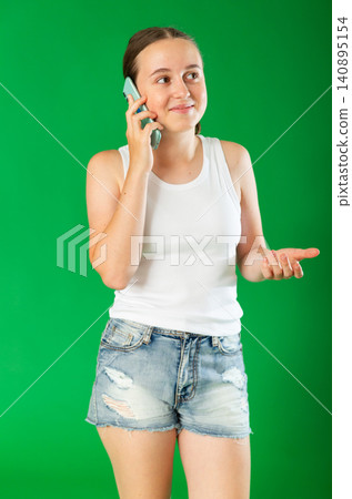 Teenage girl talking on mobile phone in front of green screen Teenage girl talking on mobile phone in front of green screen 140895154