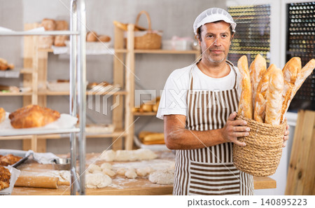 Smiling male salesman showing assortment of bakery products behind bakery counter Smiling male salesman showing assortment of bakery products behind bakery counter 140895223