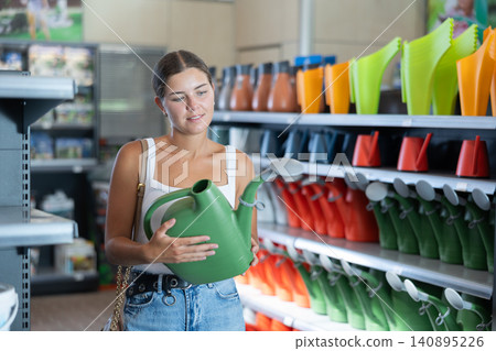Young woman choosing watering can in store Young woman choosing watering can in store 140895226
