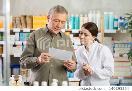 Female pharmacist helps an elderly man buy pills on doctor prescription Female pharmacist helps an elderly man buy pills on doctor prescription 140895264