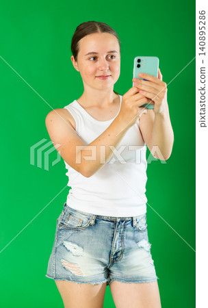 Teenage girl taking photo or scanning QR code in front of green screen Teenage girl taking photo or scanning QR code in front of green screen 140895286