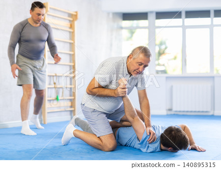 Elderly man applying armlock to opponent in mock bout at self-defense classes Elderly man applying armlock to opponent in mock bout at self-defense classes 140895315
